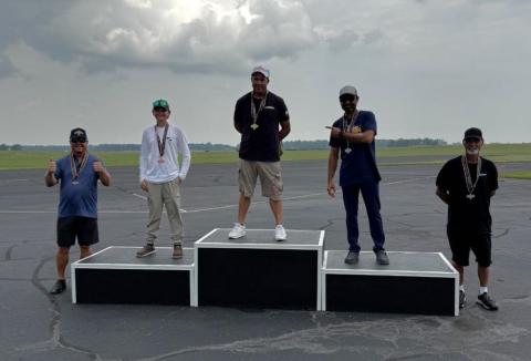 Five men on a podium outdoors, each wearing medals.