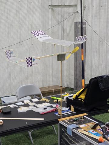 Model airplane on a stand, surrounded by tools and papers on a table in a workshop setting.