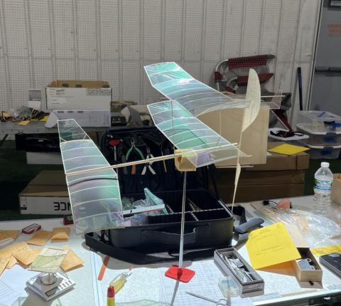 Model airplane with translucent wings on a cluttered table indoors.