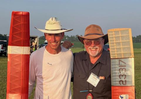 Two men smiling, standing outdoors, holding colorful model airplane wings.