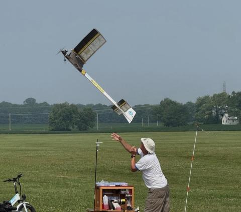 Man launching a small model airplane in a grassy field.