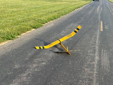 Yellow model glider with black stripes on a paved road.