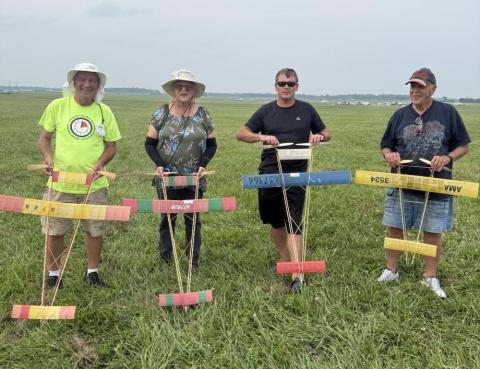 Four people holding colorful model planes in a grassy field.