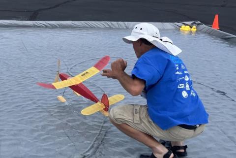 Man in blue shirt launches toy plane on water surface.