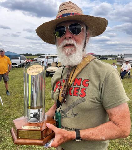 Man in sunglasses and hat holding a large trophy at an outdoor event.