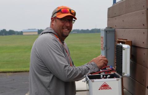 Man working outdoors with electrical equipment, smiling.
