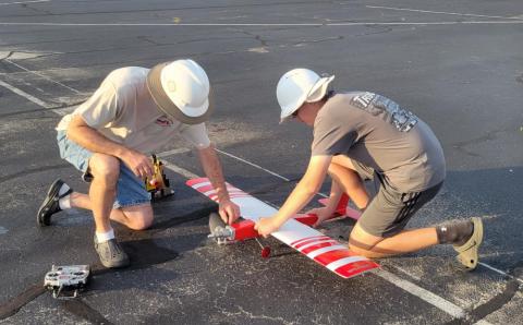 Two people adjust a red and white model airplane on the ground.