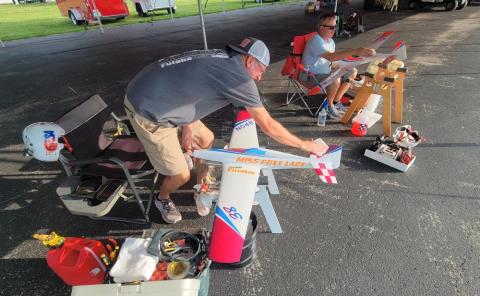 Two people preparing model airplanes under a tent.
