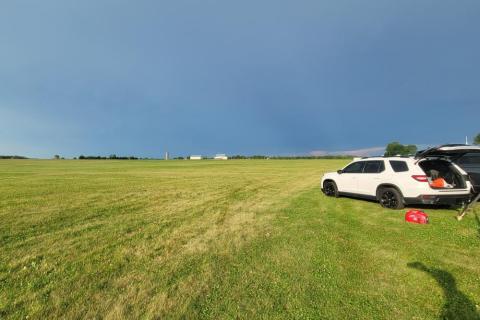 Open field under a cloudy blue sky with a parked white SUV.