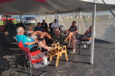 A group of people sitting in folding chairs under a canopy, conversing and relaxing.