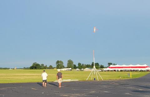 Two people watch a small plane flying vertically in a clear sky.