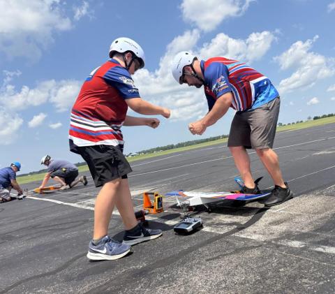 People preparing a remote-controlled airplane on a sunny runway.