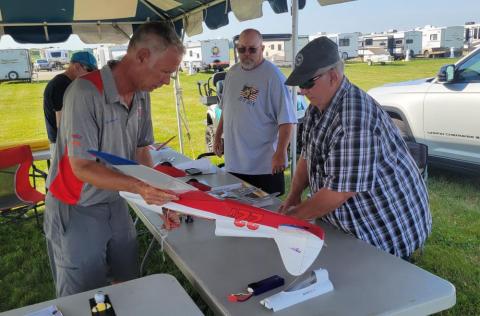 Two men assembling a model airplane at an outdoor event.