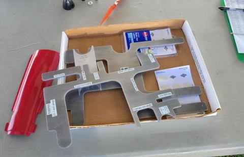 CNC machine parts on a table with papers and a red tool.