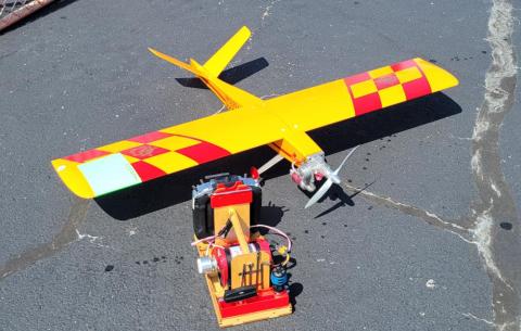 Yellow and red model airplane on pavement with engine equipment.