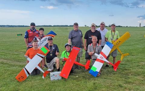 Group with model airplanes on a grassy field.