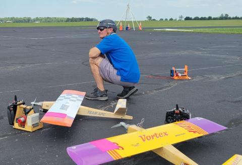 Man crouching beside model aircraft on airstrip.