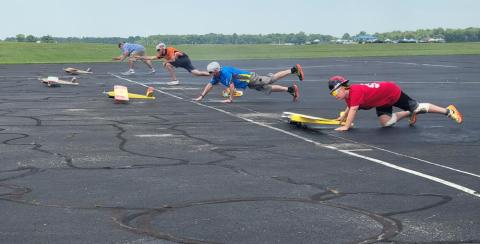 Men launching remote-controlled airplanes on a tarmac, wearing helmets.
