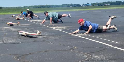 People crawling on a runway, racing toy airplanes outdoors.