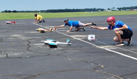 Toy planes race on a tarmac with people crouched in starting positions.