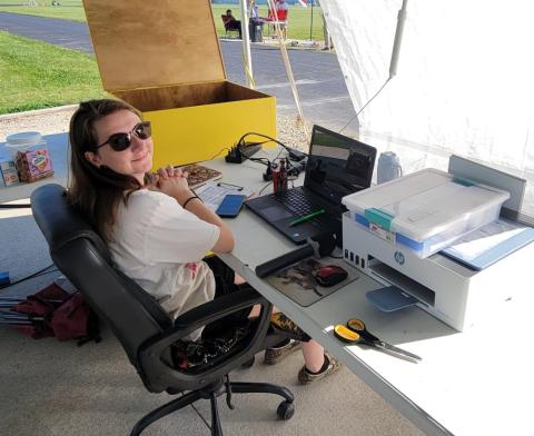 A person sitting at a desk with a laptop and printer outside.