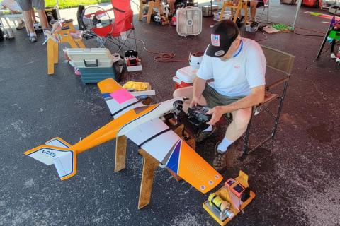Person preparing a model airplane outdoors, surrounded by tools and equipment.
