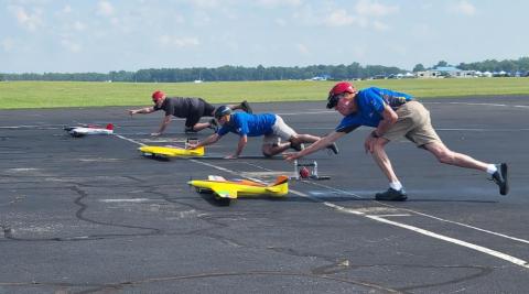 Remote-controlled airplanes being launched by four people on an airstrip.