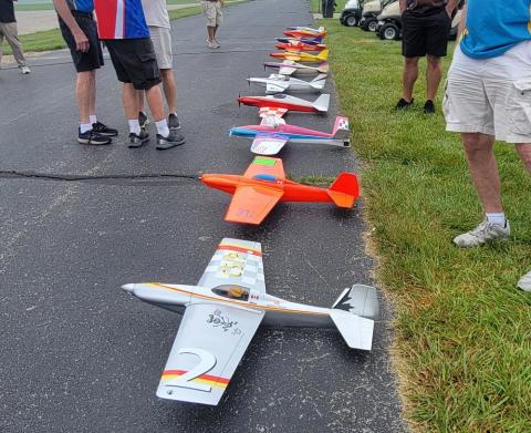 Model airplanes lined up on pavement with people standing nearby.