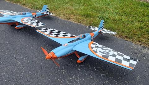 Two blue and orange model planes on pavement, featuring checkered patterns on the wings.