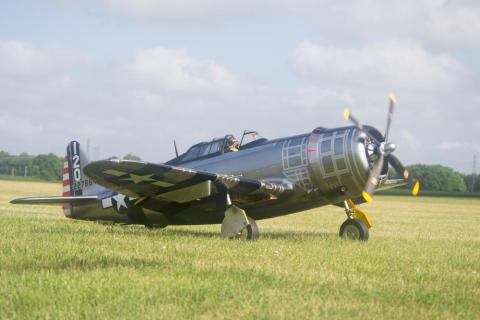 A vintage military aircraft on a grassy field under a partly cloudy sky.