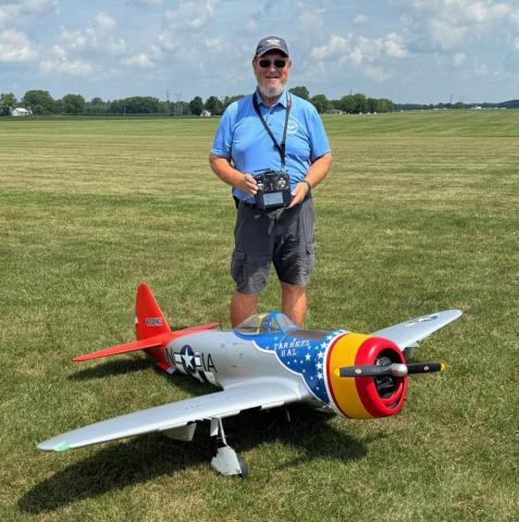 Man standing behind large model airplane on grass field.