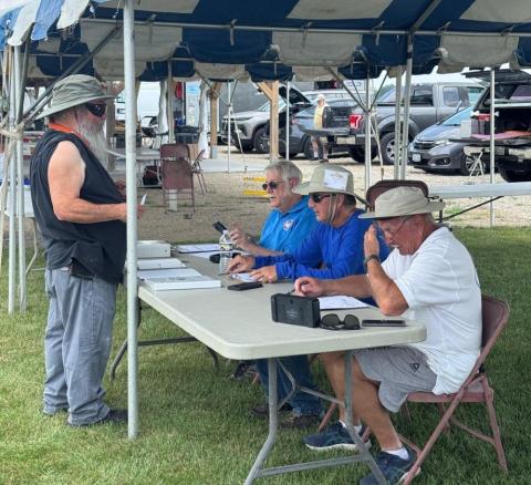 Outdoor registration table under a tent, attended by three sitting individuals.
