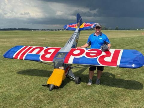 Man standing next to large remote-controlled plane on grass field.