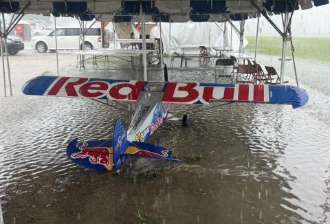 Aircraft with Red Bull logo sheltered under a tent during heavy rain.