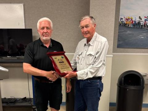 Two men shaking hands, one holding a plaque, in an office setting.