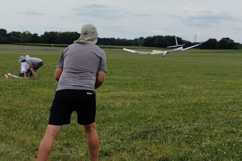 Two people flying a remote-controlled glider on a grassy field.