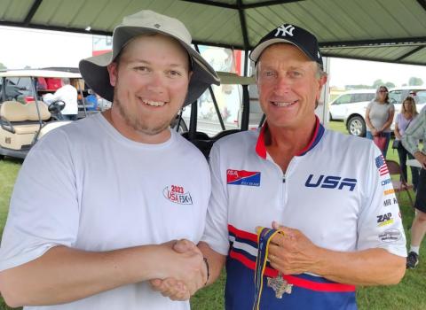 Two men smiling and shaking hands under a canopy.