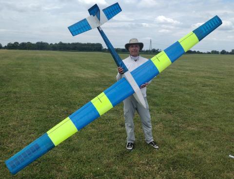 Man holding a large blue and yellow model glider on a grassy field.