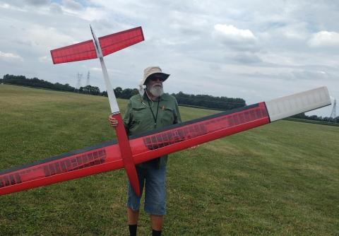Man holding a large red model airplane in a grassy field.