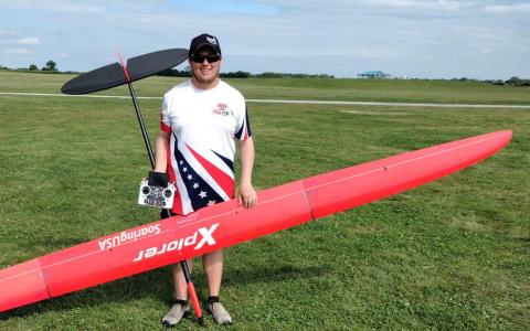 Man holding a large red model glider on a grassy field.
