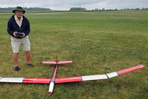 Man with remote controls large red model glider on grassy field.
