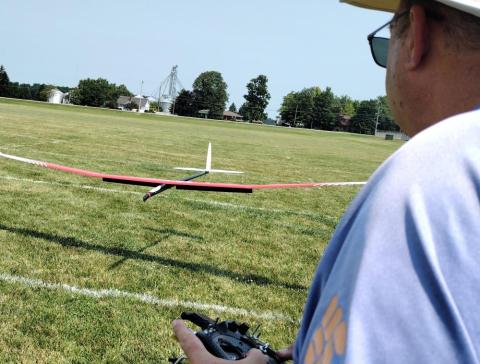 Man flying a model airplane in a park on a sunny day.