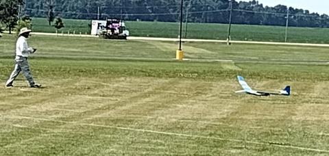 Man walking towards a small glider on a grassy field.