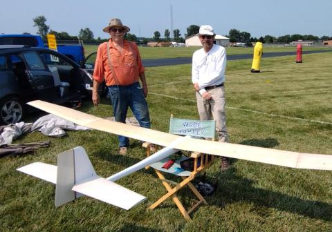 Two men standing on grass with a large model airplane.