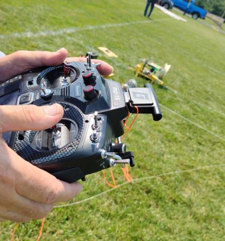 Hands holding a remote control for a drone on a grassy field.