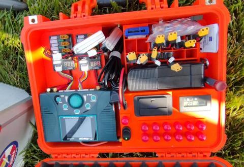 Orange equipment case with electronic components and wires on grass.