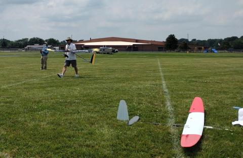 Man preparing to launch small model plane on grassy field.