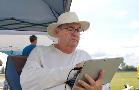 Man in a white hat using a tablet under a canopy on a sunny day.