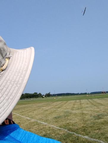 Wide-brimmed hat, field, and airplane in the sky.