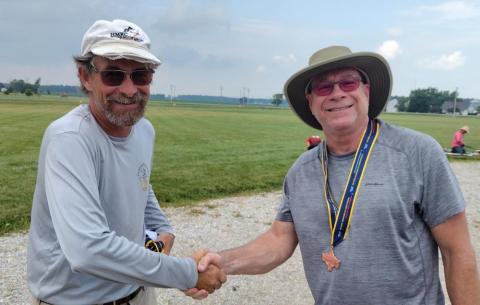 Two men shaking hands outdoors, one wearing medals.